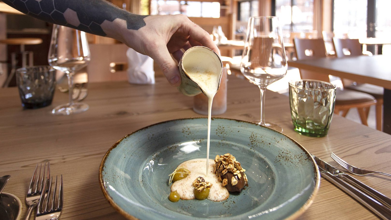 Alpin Lodges Oberjoch – Exklusive Ferienwohnungen mit Wellness Hand gießt cremige Sauce über Dessert auf blauem Teller im Restaurant